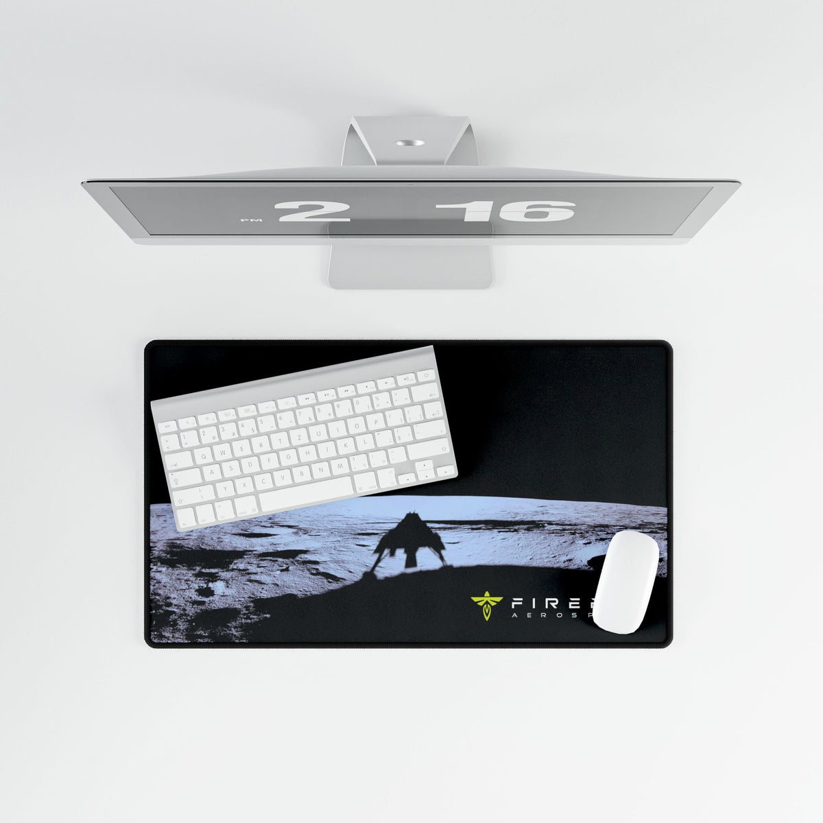 A rectangular desk mat with a black background and a graphic of a creature on a moon-like surface, shown with a white keyboard and mouse on top. A sleek silver monitor is positioned above the desk mat against a clean white background.