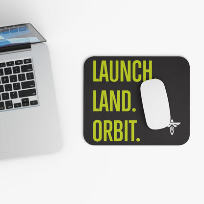 Mouse pad with 'Launch Land Orbit' text next to a laptop on a white surface