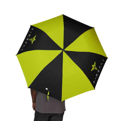 A person holding open a large umbrella with alternating bright yellow-green and black panels. The umbrella has a yellow leaf logo and the word 'FIREFLY' printed on some panels, and a small white logo near the lower edge.