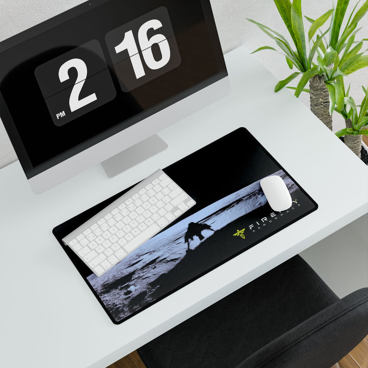 A large rectangular desk mat with a black background and a printed scenic graphic, styled on a white desk alongside a keyboard, mouse, computer monitor, and potted plant.