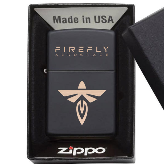 A matte black Zippo Firefly Aerospace lighter displayed inside its black presentation box, with the lid partially visible on the right. The lighter features the words 'FIREFLY AEROSPACE' and a stylized Firefly logo in a metallic gold/rose-gold finish.
